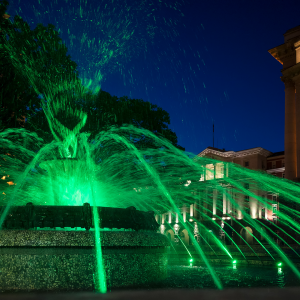 A large outdoor fountain at night with green color water streams.